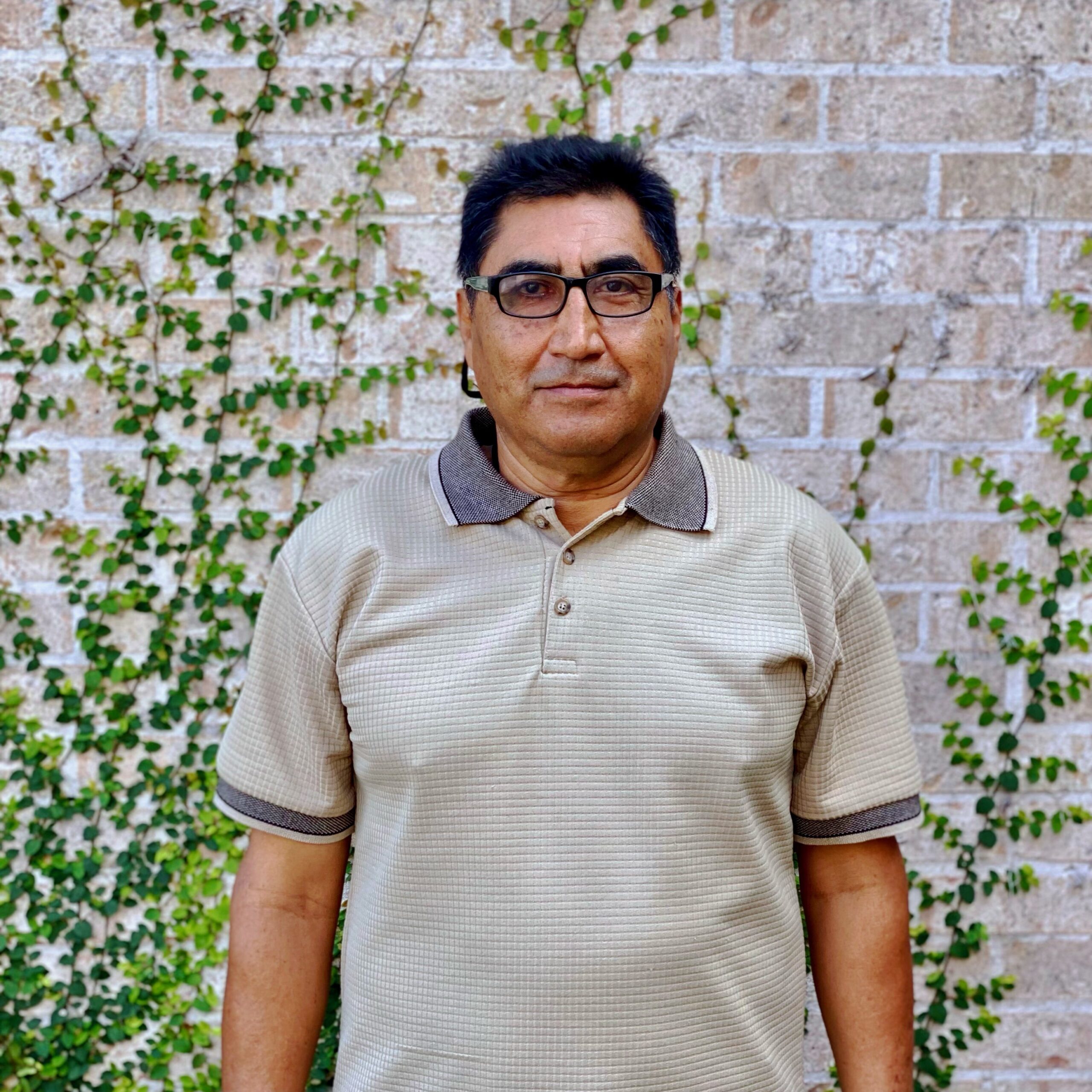 Headshot of serious Latino man in a tan polo shirt against a brick background